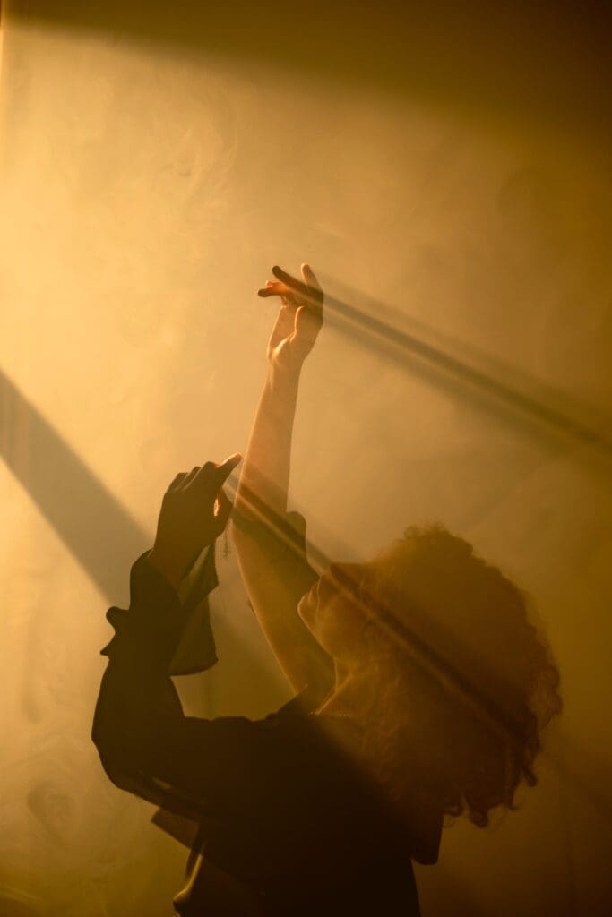 Woman enjoying Ecstatic Dance in a foggy room with decent orange light fro above.